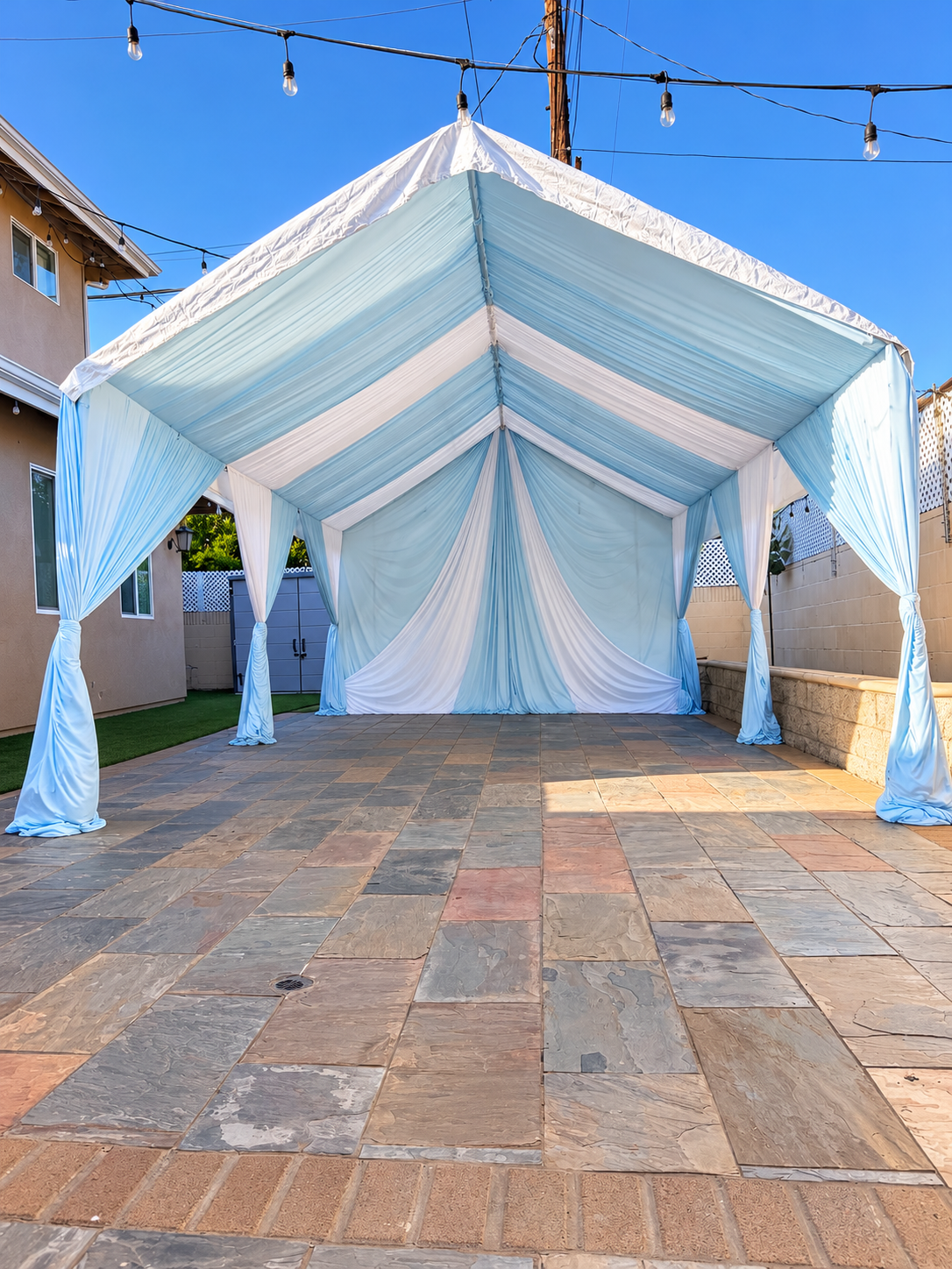 12x20 frame tent with light blue and white draping on a paved patio